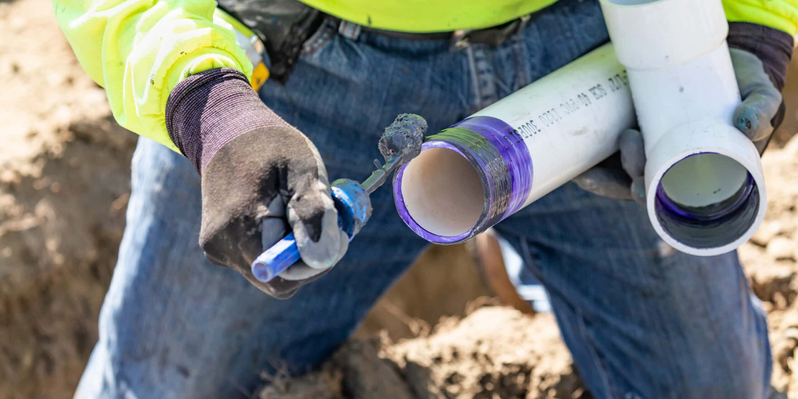Plumber Applying Pipe Cleaner, Primer and Glue to PVC Pipe At Construction Site.